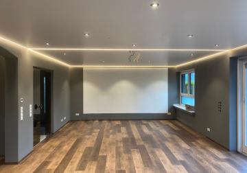 Großes Wohnzimmer mit Spanndecke, umlaufender Lichtvoute, Einbauspots sowie Beamer-Zuleitungen und vorbereiteter Halterung.